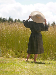 Woman seen from back wearing a brown kimono with white lines and large straw hat with summer field in background