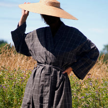 Load image into Gallery viewer, Close-up of woman wearing brown checked khadi kimono and large straw hat with summer field background