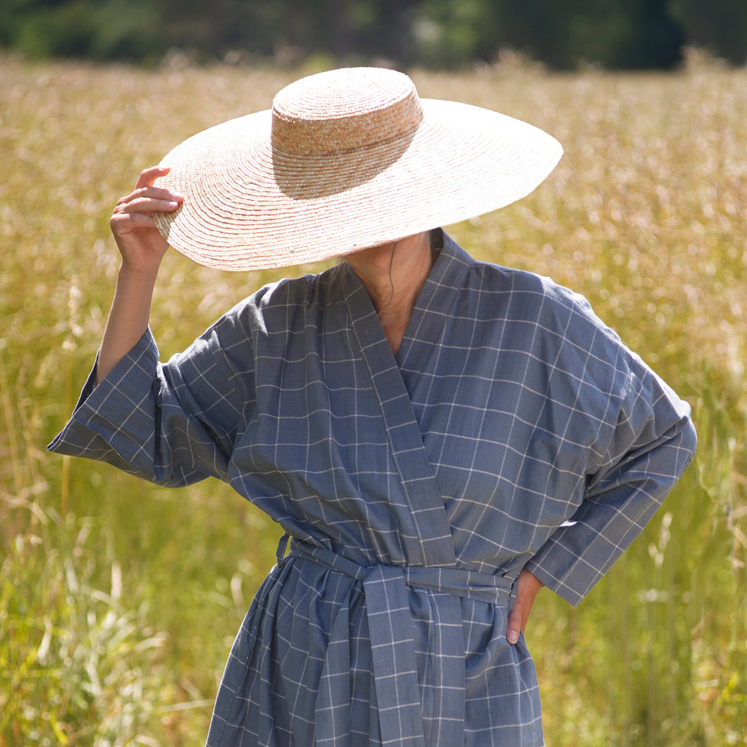 Woman wearing dove blue grey kimono with checks and large straw hat with a summer field background