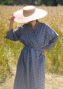 Woman wearing dove blue grey long kimono with checks and large straw hat with a summer field background