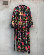 Load image into Gallery viewer, Back side of a colorful black floral-patterned dress hanging against a gray concrete wall
