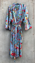 Load image into Gallery viewer, Colorful light blue robe with floral and bird pattern hanging on a concrete wall.