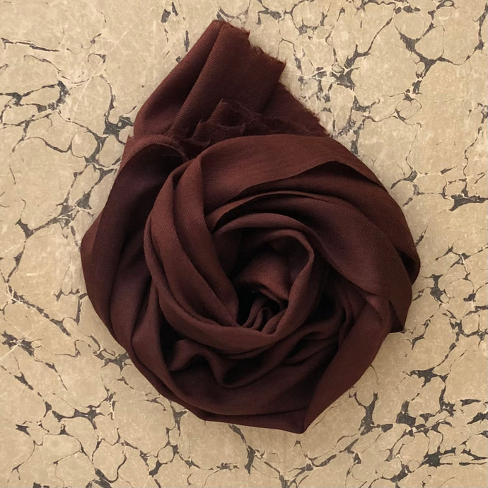 Cashmere scarf in chocolate brown rolled on marbled background