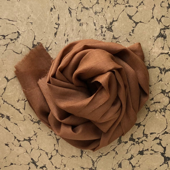 Cashmere scarf in cinnamon brown rolled on marbled background