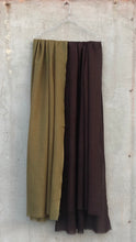 Load image into Gallery viewer, Two pairs of scarves, one olive green and one brown, hanging on a hanger against a concrete wall.