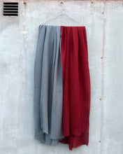 Load image into Gallery viewer, Two wool scarves, one gray and one red, hanging on a concrete wall.