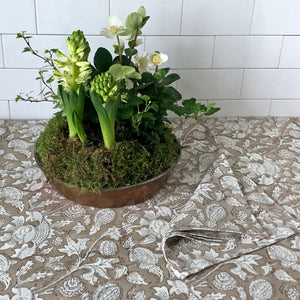 Block printed tablecloth and napkin with beige ground and white flowers. White hyacints in copper pot.