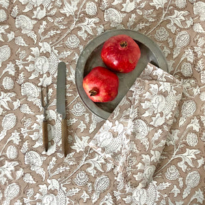 Block printed tablecloth and napkin with beige ground and white flowers. Two pomegranates on pewter plate.