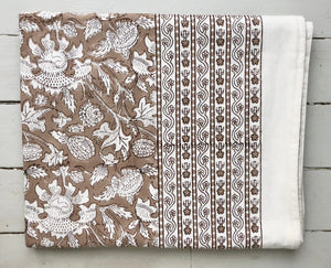 Block printed tablecloth with beige ground and white flowers, folded with visible matching border.