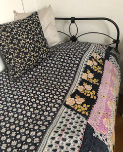 Quilt with floral patterns on a bed with a black metal frame.