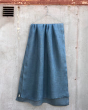 Load image into Gallery viewer, Dusty blue linen scarf hanging against a textured concrete wall.