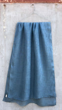 Load image into Gallery viewer, Dusty denim blue linen scarf hanging against a textured concrete wall.