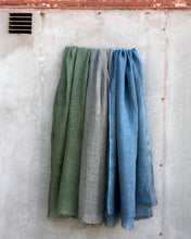 Load image into Gallery viewer, Three linen scarves in green, gray, and blue hanging against a textured wall.