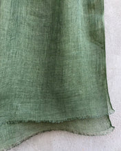 Load image into Gallery viewer, Close-up of sage green linen scarf against a textured concrete wall.