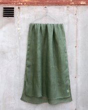 Load image into Gallery viewer, Sage green linen scarf hanging against a textured concrete wall.