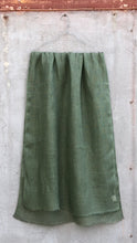Load image into Gallery viewer, Sage green pure linen scarf hanging against a textured concrete wall.